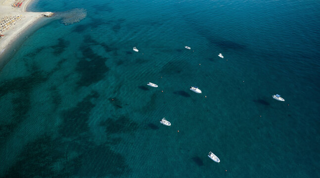 Aerial view of a group of speedboats surrounded by a transparent blue sea moored in front of a beach in Isca sullo Ionio, Calabria, Italy.