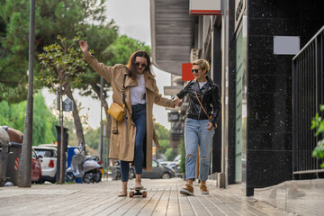 Two adult women learn to ride skateboard in a city. Urban lifestyle scene in Barcelona.