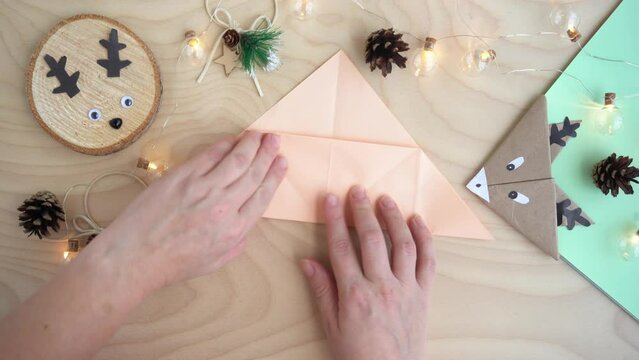 Top view, women's hands make a bookmark out of paper in the origami technique, a craft deer.New Year and Christmas concept. DIY gift wrapping