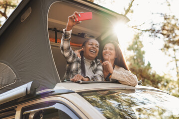 Senior multracial female friends having fun during road trip while taking a selfie with mobile...