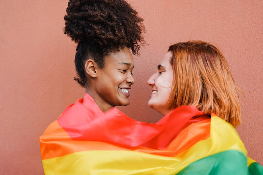 Happy gay women couple having tender moment while wearing LGBT rianbow flag at pride parade