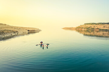 Caucasian female tourist float on dead sea water happy enjoy vacation in Jordan. Sunset panorama with person in salty lake water