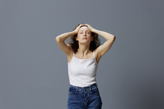 Tired Relaxing Calm Curly Beautiful Woman In Basic White T-shirt Enjoys Head Massage Closing Eyes Posing Isolated On Over Gray Blue Background. People Lifestyle Emotions Concept. Copy Space