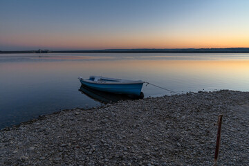 sunset over Lake Budeasa in central Romania with a wooden rowboat tied up on the rocky beach