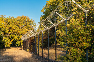 view of a tall fence with barbed wire leading through forest on the border of Turkey and Bulgaria