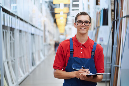 Smiling Salesman Of A Flooring Store Standing In A Hall With Laminate Samples.