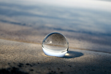 Glazen lensbal op het strand als gevolg van het meer en de lucht. Concept van rust en zen.