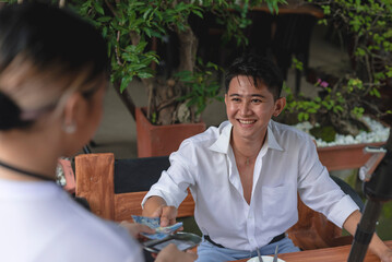 A handsome young and dapper man pays the bill for his food at an alfresco restaurant. Paying in...