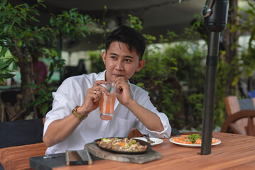 A handsome young man sips his cold drink as he dines in an al fresco restaurant with sisig and...