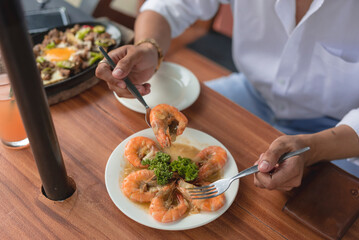 A dish of scrumptious garlic buttered shrimp topped with parsley and served in an outdoor restaurant. A guy scoops a piece of shrimp with a spoon and fork before eating it.