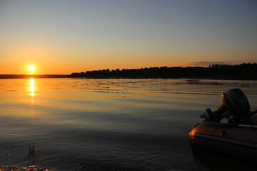 Inflatable rubber boat with a motor near the shore, on the lake in the evening