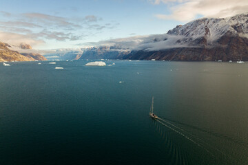 Aerial view of a sailing boat navigating along the fjords in Sermersooq, Greenland.