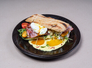 Delicious freshly prepared breakfast on black plate. Fried eggs on bacon. Toasted bread. Cherry tomatoes, arugula.