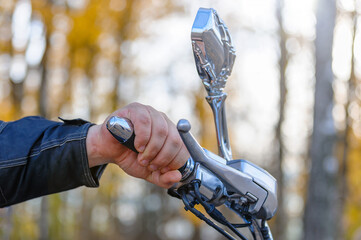 The biker's hand in selective focus is holding the steering wheel of a motorcycle.