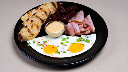 Fresh tasty english breakfast on beautiful black plate. Bacon, fried eggs and sausages, sauce, toasted bread.