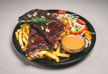 Delicious freshly prepared food on beautiful black plate.. French fries, barbecued ribs with...