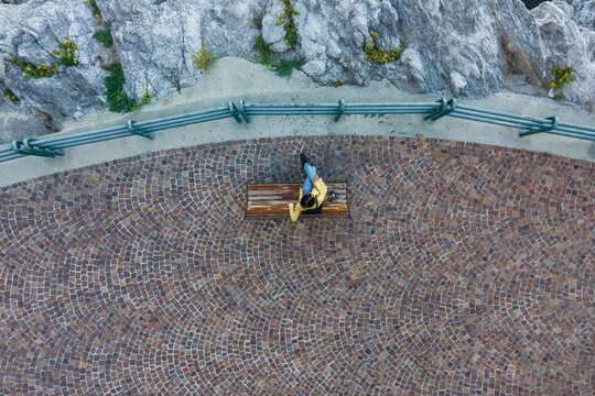 Aerial view of a woman sitting on the bench at waterfront in Erchie, Amalfi Coast, Salerno, Campania, Italy.