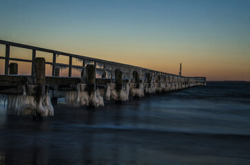 Obraz premium frozen sea bridge at sunset II, Bücke in der Ostsee mit Eiszapfen bedeckt bei Sonnenaufgang in Germany