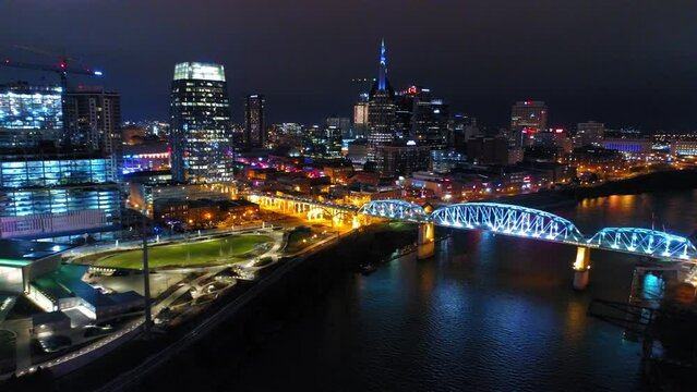 Aerial Shot Of Pedestrian Bridge In Sparkling City, Drone Flying Backwards Over Cumberland River At Night - Nashville, Tennessee