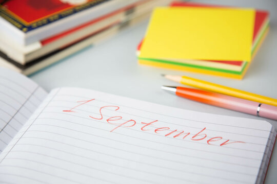 An open notebook with the inscription - the first of September, is on the table next to books and school supplies. The topic is First day of school.