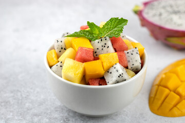 Fruit salad with mango, watermelon, dragon fruit, pineapple, mint on a gray background. Thai tropical fruit salad.