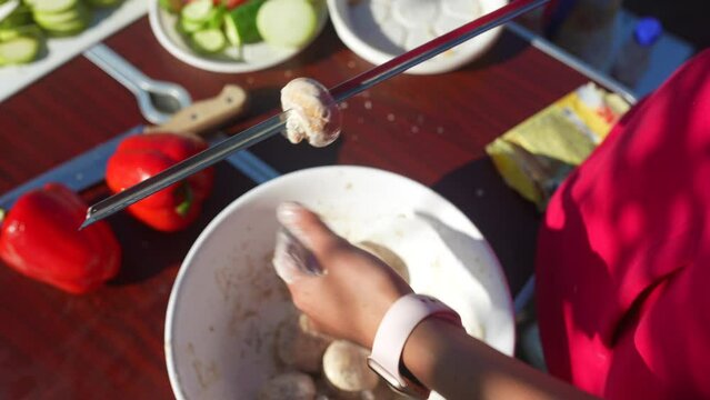 Woman stringing champignons on a skewer, close view. Meat substitute.