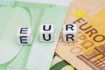 Small white beads with letters EUR on pile of euro banknotes, closeup detail