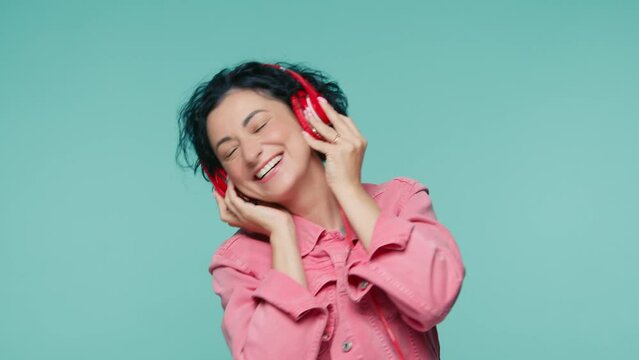 Mature woman with short curly hairs dancing on green background. Female having fun when listening music. 40s model smiling openly with nice white teeth.Female moves to rhythm of music positive footage