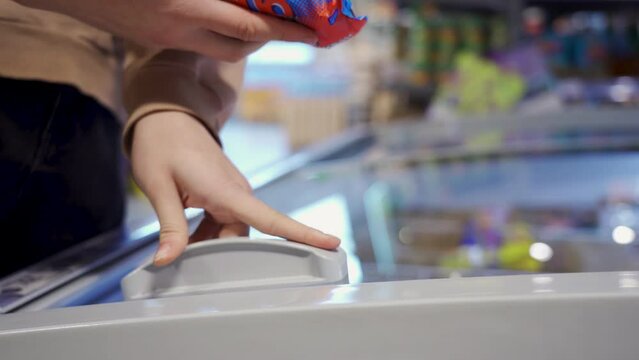 Female hands opening glass door in the refrigerated section at the supermarket and choosing ice cream.