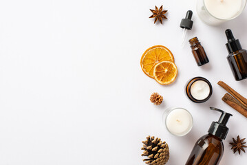 Organic cosmetics concept. Top view photo of amber glass bottles candles pine cones cinnamon sticks anise and dried orange slices on isolated white background with copyspace
