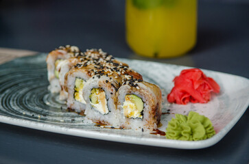 Appetizing portion of sushi rolls philadelphia with eel, with soft cheese, cucumbers, avocado and ginger with wasabi, on a gray plate on a black table, on the background of yellow fruit juice