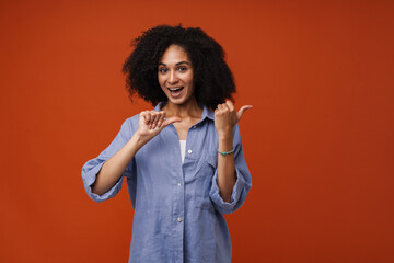 Young beautiful smiling curly woman pointing aside both thumb fingers