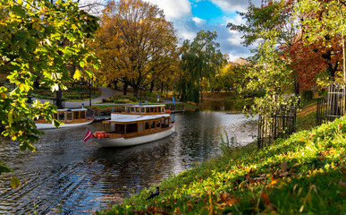 Beautiful view to the city canal through park with autumn colorful trees. Tourist boat in the canal