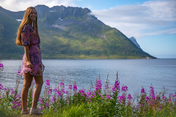 a long-haired girl in a colourful dress enjoys the sunny weather on the island of senja, norway,...