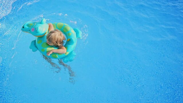 Happy little boy circling in pool sitting in inflatable ring, swimming in street pool in courtyard. Joyful baby. Tropical resort. Family beach vacation.