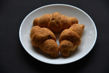 French croissants on a white plate. Delicious and sweet bread croissants. Sweet breakfast on a black background. European cuisine.