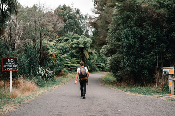 sporty young man with long hair tied back in a bun walking on nature park entrance road with...