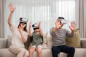 Moment happy of Asian family father, mother, and daughter wearing VR 3d or virtual reality glasses headset technology playing video game together on sofa living room at home.