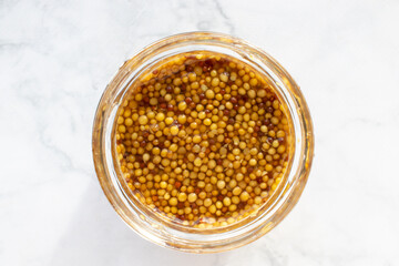 Mustard seeds sauce in glass jar on marble table background. Top view, copy space