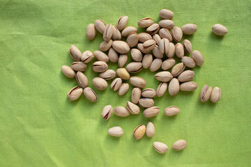 Pistachio nuts on green table cloth background. Close up, top view, copy space. Healthy snack