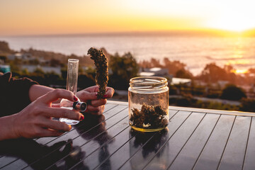 Hands with red nails holding a big marijuana bud (weed head), glass jar with more marijuana buds,...