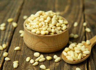 Heap of raw pine nuts in a wooden bowl and spoon. Peeled pine nuts on an old wooden table.