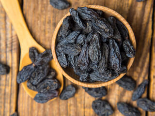 Black raisins in a wooden bowl on a textured old wood background. copy space.
