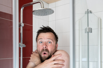 Man in the shower under cold water, he freezes and looks miserable. Energy crisis concept.