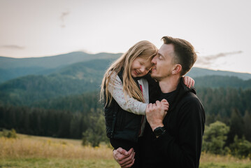 Child hugging father and playing in the park at the sunset time. Concept of friendly family. Father's Day. Portrait dad and daughter on summer or autumn vacation. Place for text, advertising. Closeup.