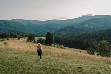 Child in autumn mountains. Girl is running on the grass in the field and enjoying nature. Little hiker and traveler walk on top of foggy mountain. World Tourism Day. Active outdoor games. Back view.