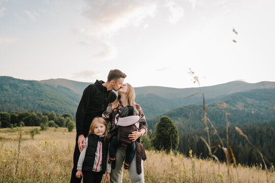 Family with kids hiking in mountains. Young tourists on top of a mountain enjoying valley view sunset. Mom, and dad with a backpack son and daughter. Holiday trip concept. World Tourism Day.