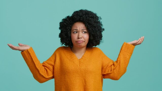 Difficult question facial expression lifestyle people concept. Blue studio isolated background 4K. Young indifferent unsure African American woman makes gesture of I do not know, can not help anything