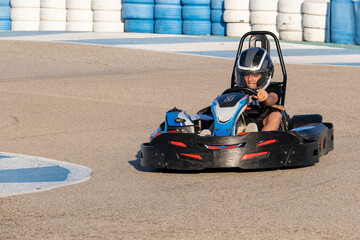 a teenager boy driving a kart at the exit of a curve of a karting circuit, face of speed and concentration while driving a go kart - obrazy, fototapety, plakaty