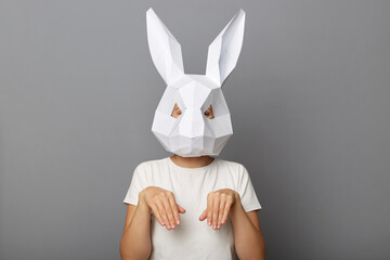 Portrait of funny unknown female wearing bunny mask and white t-shirt standing with hare paws,...